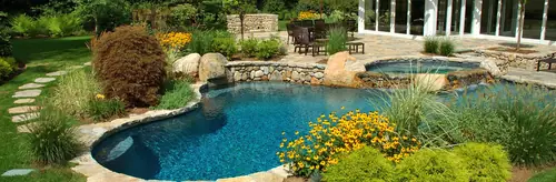 A freeform pool and raised spa edged with boulders, ornamental grasses and yellow coneflowers
