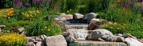 A rock water feature edged with day lilies, ornamental grasses and flowering perennials